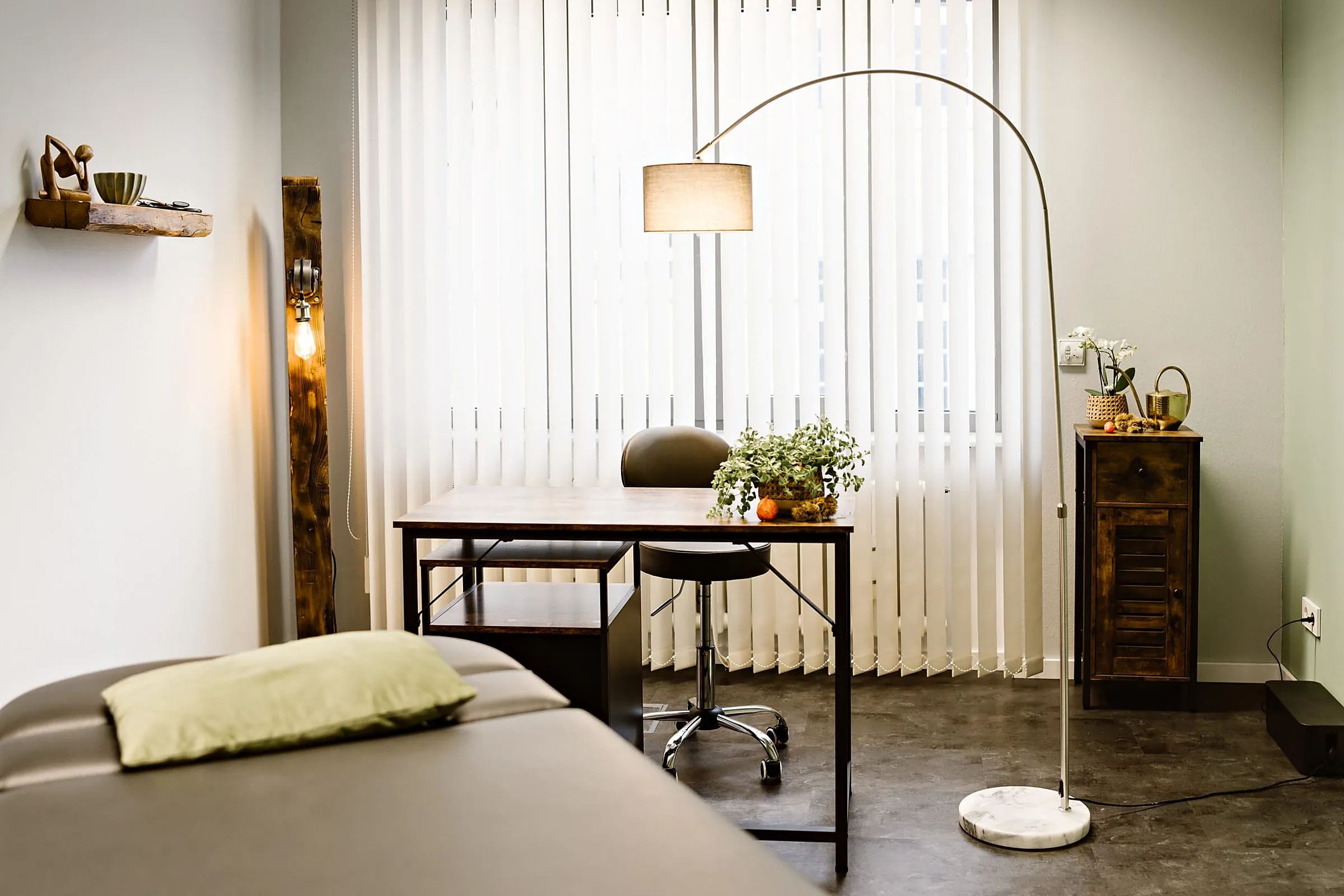 Heller Behandlungsraum mit Liege, Schreibtisch und Pflanzen